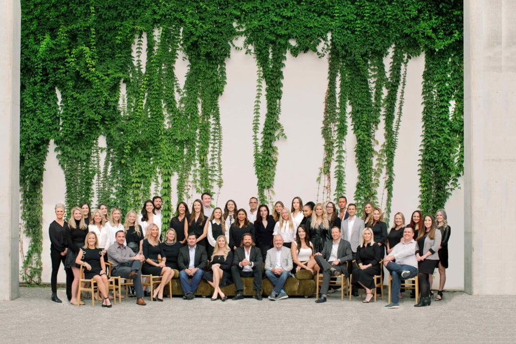 Large group of people posing in front of a wall with greenery