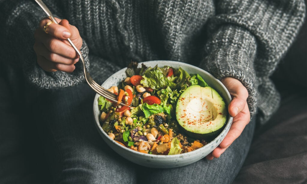 Person holding a salad bowl with avocado, tomatoes, and greens